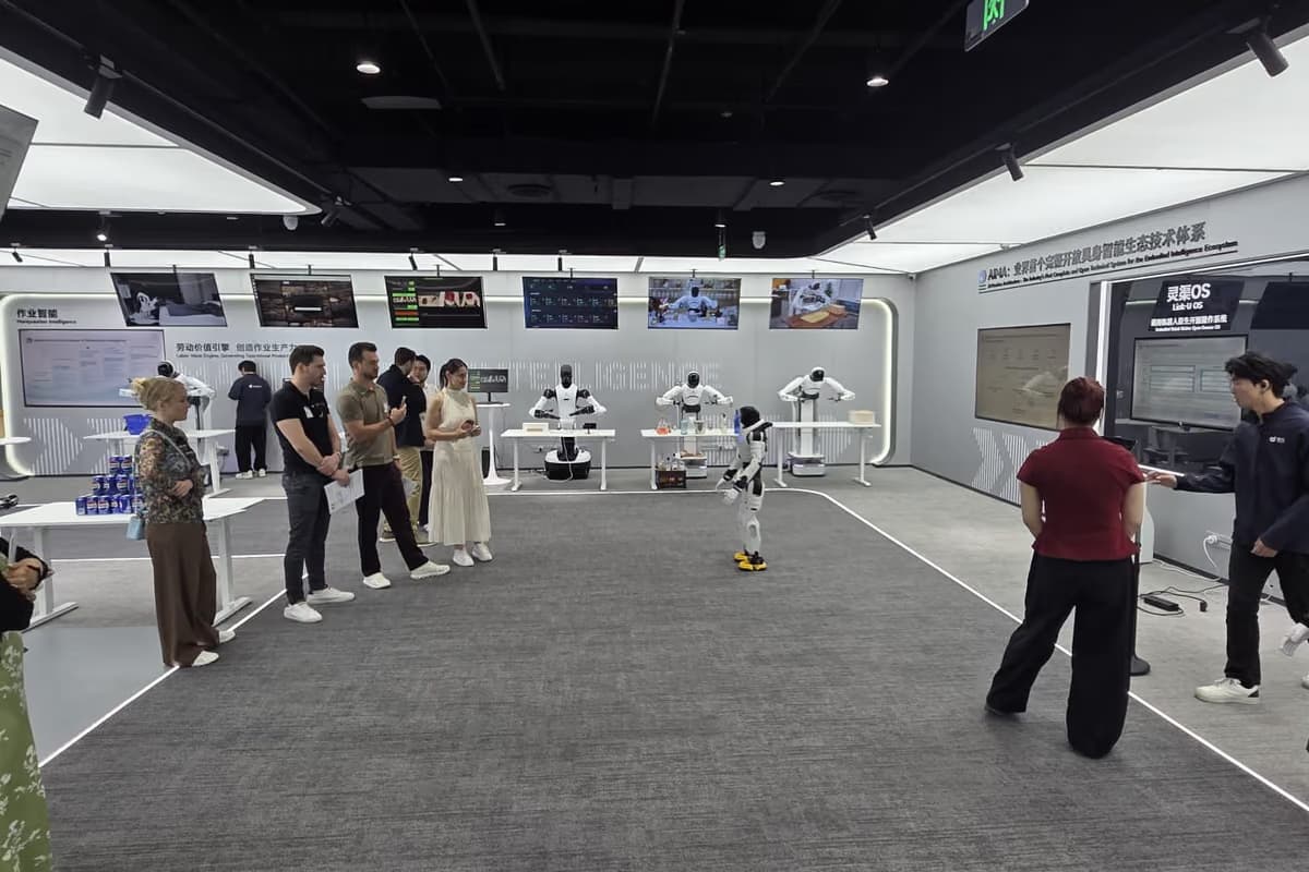 Ein weiter, heller Raum mit Bildschirmwänden, links eine Besuchergruppe, in der Mitte zwei humanoide Roboter.