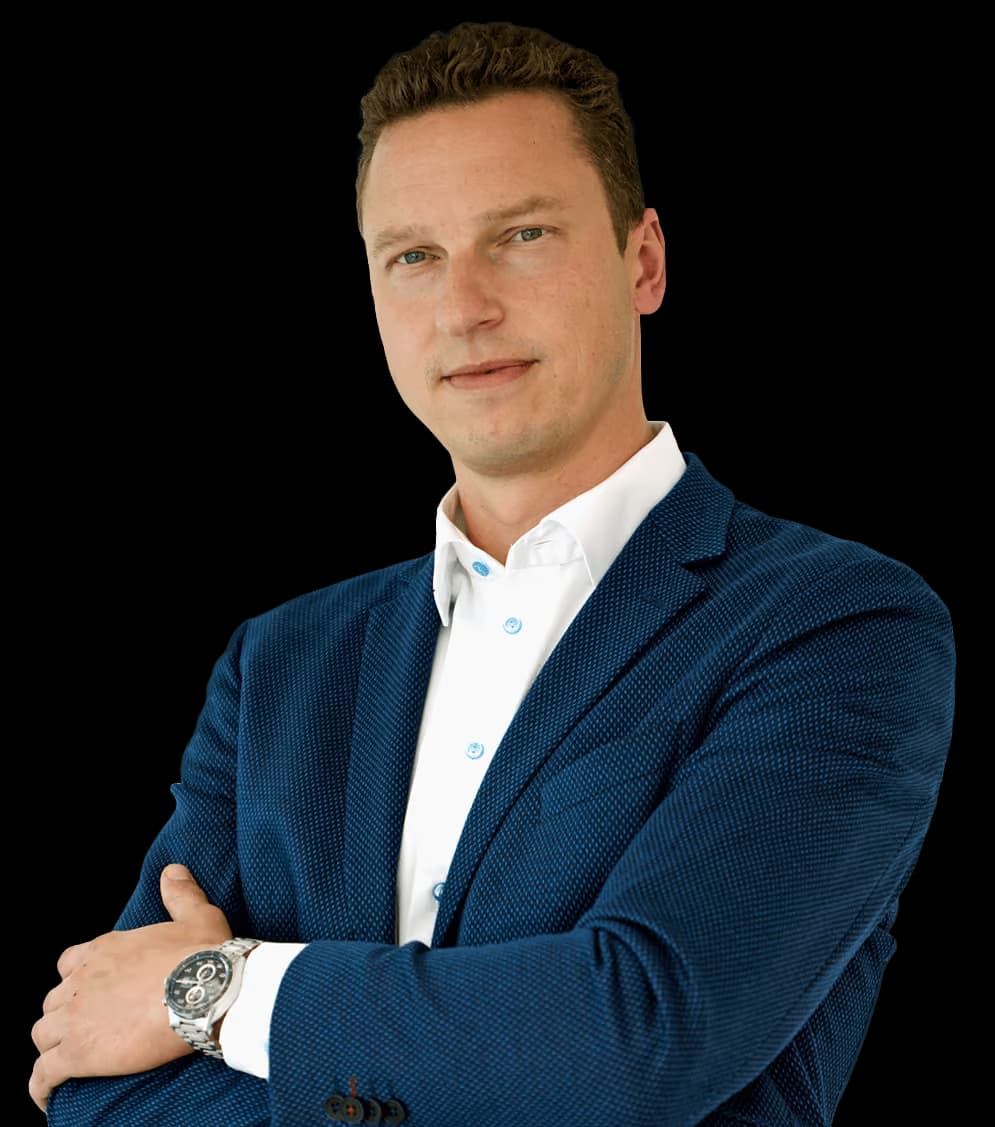 Mathias Dögel im dunkelblauen Sakko über weißem Hemd, mit verschränkten Armen vor weißem Hintergrund.